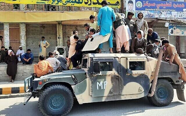 مقاتلو طالبان والسكان المحليون يجلسون على عربة همفي تابعة للجيش الوطني الأفغاني على جانب الطريق في ولاية لغمان، 15 أغسطس 2021 (AFP)