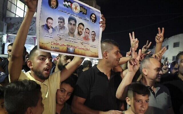 فلسطيني يرفع  ملصقا يحمل صور الأسرى الفلسطينيين الستة الذين فروا من سجن اسرائيلي خلال احتفالات  في مخيم جنين للاجئين في شمال الضفة الغربية، 6 سبتمبر، 2021. (Jaafar Ashitiyeh / AFP)