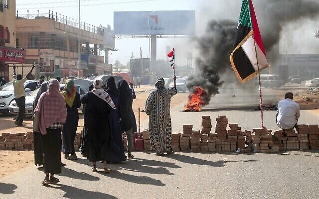 متظاهرون سودانيون يرفعون الأعلام السودانية بجوار حاجز من الطوب خلال مظاهرة في العاصمة الخرطوم ، في 25 أكتوبر ، 2021، للتنديد باعتقالات الجيش لأعضاء الحكومة السودانية ليلا. (AFP)