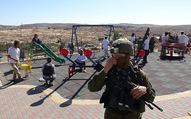 جندي إسرائيلي يقف جانبا بينما يقوم مستوطنون إسرائيليون بدخول ساحة لعب فلسطينية في قريا سوسيا بالضفة الغربية، 6 نوفمبر، 2021.  (Credit: Guy Butuvia)