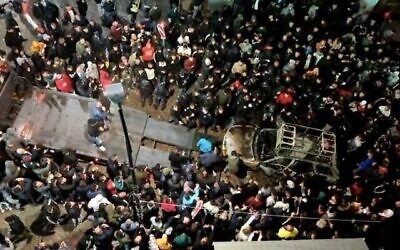عشرات الفلسطينيين يقفون حول سيارة إسرائيلية محترقة قادها إسرائيليان إلى وسط مدينة رام الله يوم الأربعاء، 1 ديسمبر، 2021. (Screenshot: Facebook Live)