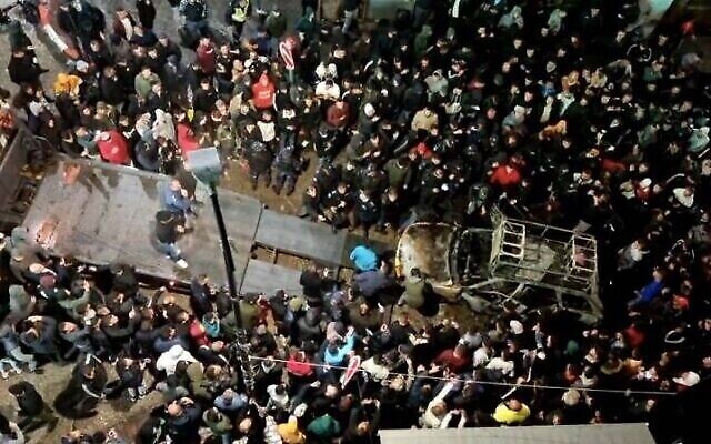 عشرات الفلسطينيين يقفون حول سيارة إسرائيلية محترقة قادها إسرائيليان إلى وسط مدينة رام الله يوم الأربعاء، 1 ديسمبر، 2021. (Screenshot: Facebook Live)