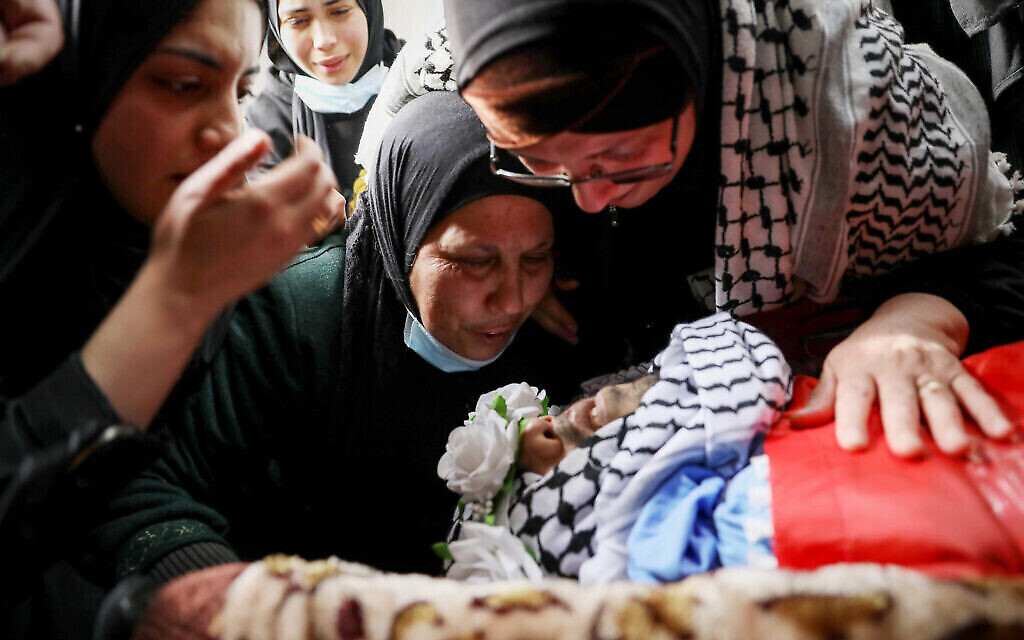 فلسطينيون يقفون فوق جثمان عمار شفيق أبو عفيفة، الذي قُتل برصاص قوات الجيش الإسرائيلي بالقرب من بلدة بيت فجار، خلال جنازته في مخيم العروب للاجئين بالقرب من مدينة الخليل بالضفة الغربية، 2 مارس، 2022.  (Wisam Hashlamoun/ Flash90)