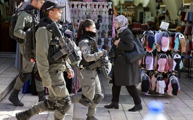 امرأة فلسطينية تمر أمام قوات أمن إسرائيلية تقوم بدورية في البلدة القديمة في القدس، 31 مارس 2022 (Menahem KAHANA / AFP)