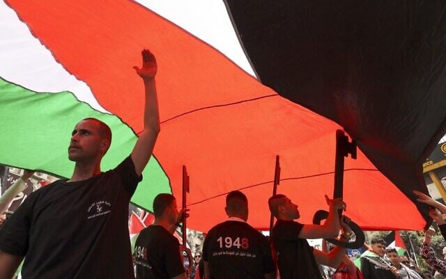 فلسطينيون  يلوحون بالأعلام الفلسطينية ويحملون نماذج مفاتيح عملاقة (رمز يستخدم على نطاق واسع للنكبة ، حيث احتفظ العديد من الفلسطينيين بمفاتيح منازلهم عندما أجبروا على النزوح في عام 1948)، خلال مسيرة لإحياء الذكرى الـ 74 للنكبة، في مدينة رام الله الضفة الغربية، 15 مايو، 2022. (ABBAS MOMANI / AFP)