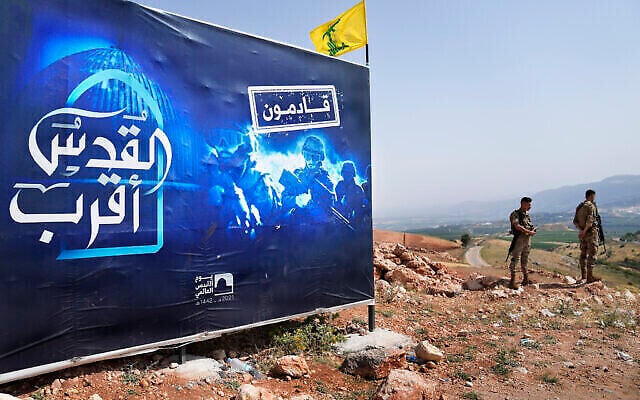 جنود الجيش اللبناني يقفون بجانب لوحة إعلانية تظهر مقاتلي حزب الله كتب عليها: "القدس أقرب، قادمون" ، التي تقع على تل مقابل بلدة المطلة الإسرائيلية، على الحدود اللبنانية الإسرائيلية، بالقرب من قرية كفركلا اللبنانية، 29 مايو 2022 (AP / Hussein Malla)