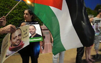 متظاهرون يحملون العلم فلسطيني خارج المستشفى في بئر يعقوب حيث السجين الأمني المضرب عن الطعام، خليل عواودة (يظهر في الصور التي يحملها المتظاهرون)، الذي تحتجزه إسرائيل، في حالة صحية متدهورة ، 13 أغسطس، 2022.  (AP/Tsafrir Abayov)