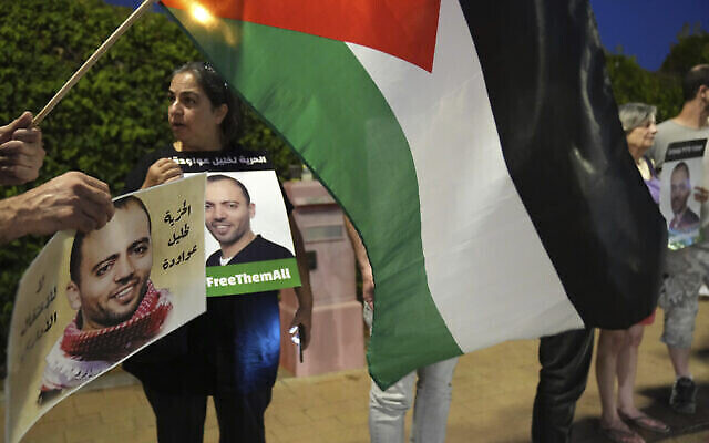 متظاهرون يحملون العلم فلسطيني خارج المستشفى في بئر يعقوب حيث السجين الأمني المضرب عن الطعام، خليل عواودة (يظهر في الصور التي يحملها المتظاهرون)، الذي تحتجزه إسرائيل، في حالة صحية متدهورة ، 13 أغسطس، 2022.  (AP/Tsafrir Abayov)