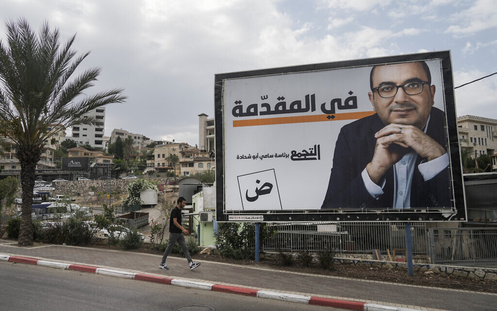 رجل يمر من أمام لوحة إعلانية لحملة انتخابية تحمل صورة سامي أبو شحادة، رئيس حزب التجمع الوطني، في مدينة أم الفحم شمال إسرائيل، الجمعة 21 أكتوبر، 2022. (AP / Mahmoud Elean)