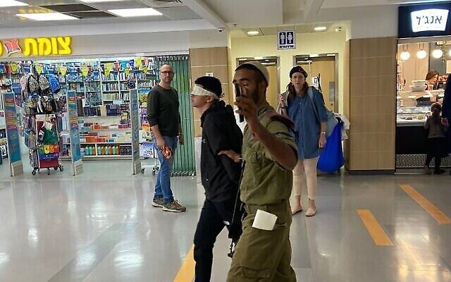 جندي إسرائيلي يرافق فتى فلسطيني معصوب العينين ومقيّد اليدين في مستشفى شعاري تسيديك في القدس، 24 أكتوبر، 2022. (Courtesy; Used in accordance with Clause 27a of the Copyright Law)