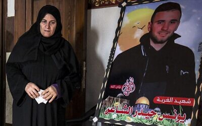 سميرة (55 عاما)، والدة الفلسطيني يونس الشاعر، واحد من ثمانية شبان فلسطينيين غرقوا قبل شهرين قبالة الساحل التونسي في محاولة الهجرة إلى أوروبا، إلى جانب صورة لابنها في منزلها في رفح جنوب قطاع غزة، 20 ديسمبر 2022 (SAID KHATIB / AFP)