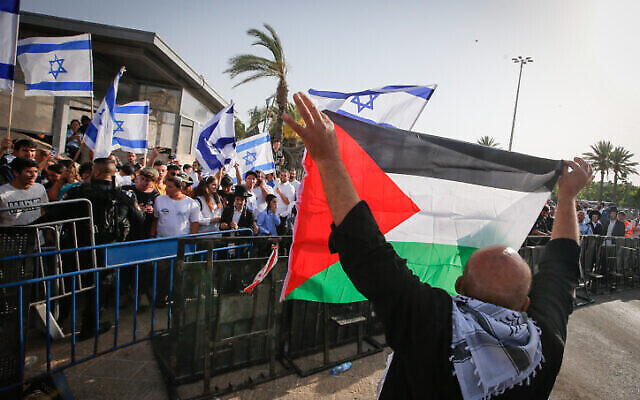 رجل يحمل العلم الفلسطيني يقف أمام متظاهرين يرفعون الأعلام الإسرائيلية بالقرب من البلدة القديمة في القدس خلال احتفالات "يوم أورشليم"، 29 مايو، 2022. (Jamal Awad / Flash90) رجل يحمل العلم الفلسطيني يقف أمام متظاهرين يرفعون الأعلام الإسرائيلية بالقرب من البلدة القديمة في القدس خلال احتفالات "يوم أورشليم"، 29 مايو، 2022. (Jamal Awad / Flash90)