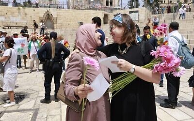 ناشطة في مجال التعايش من "تاغ مئير" تعطي زهرة لسيدة مسلمة خلال "مسيرة الزهور" السنوية التاسعة للمنظمة عبر البلدة القديمة في القدس والتي تهدف إلى نشر رسالة "الحب والاحتواء والتضامن" قبل "مسيرة الأعلام" ذات الطابع القومي المتشدد في القدس، 18 مايو، 2023.(Yossi Zamir/Tag Meir)