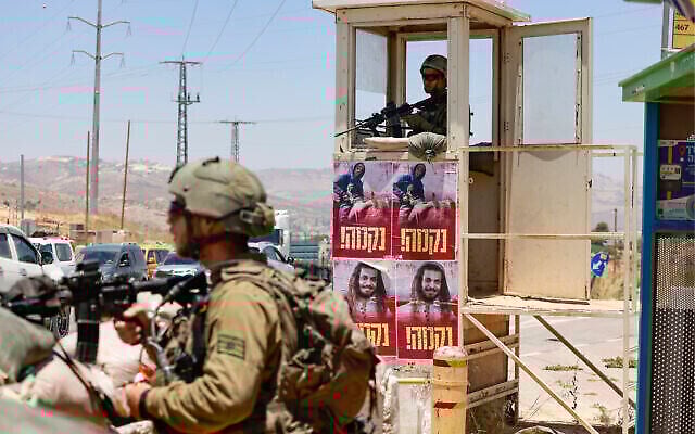 ملصقات تحمل صور إسرائيليين قُتلوا مؤخرًا على يد مسلحين فلسطينيين، كُتب تحتها كلمة "انتقام" بالعبرية ، على محطة للحافلات يحرسها الجنود الإسرائيليون عند مفرق تبواح في الضفة الغربية، 25 يونيو، 2023. (Menahem Kahana/AFP) ملصقات تحمل صور إسرائيليين قُتلوا مؤخرًا على يد مسلحين فلسطينيين، كُتب تحتها كلمة "انتقام" بالعبرية ، على محطة للحافلات يحرسها الجنود الإسرائيليون عند مفرق تبواح في الضفة الغربية، 25 يونيو، 2023. (Menahem Kahana/AFP)