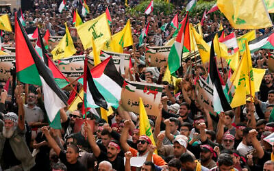 أنصار حزب الله يلوحون بالأعلام اللبنانية والفلسطينية ورايات المنظمة ويحملون لافتات مؤيدة لغزة خلال احتجاج لإظهار تضامنهم مع الفلسطينيين، في الضاحية الجنوبية في بيروت، لبنان، الجمعة، 13 أكتوبر، 2023. (AP/Hussein Malla)