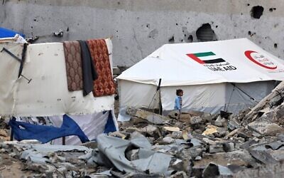 طفلة فلسطينية تسير وسط الركام أمام خيمة تحمل شعار الهلال الأحمر الإماراتي وإشارة إلى المساعدات الإماراتية، في مخيم مؤقت يأوي النازحين الفلسطينيين في رفح جنوب قطاع غزة، 28 يناير، 2024. (Mohammed ABED / AFP)