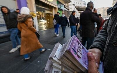 صراف يحمل رزمًا من الليرة السورية في أحد شوارع دمشق في 16 ديسمبر 2024. (Louai Beshara / AFP)