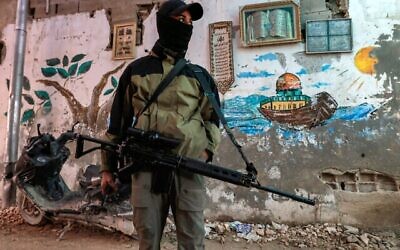 مسلح فلسطيني يقف حارسا حاملا بندقية هجومية على طول زقاق في مخيم جنين في شمال الضفة الغربية،  29 ديسمبر، 2024. (Jaafar Ashtiyeh/AFP)