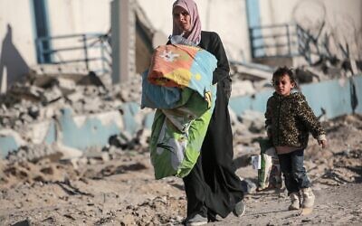 امرأة فلسطينية وطفل يحملان أمتعتهما وسط أنقاض الامباني في حي مدمر بمدينة رفح جنوب قطاع غزة، في 20 يناير 2025. (BASHAR TALEB / AFP)