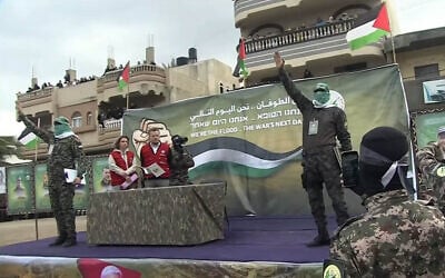 موظفو الصليب الأحمر يقفون مع مسلحين على المنصة التي أعدتها حركة حماس لتسليم الرهائن في دير البلح بقطاع غزة، 8 فبراير، 2025. (YouTube Screenshot)