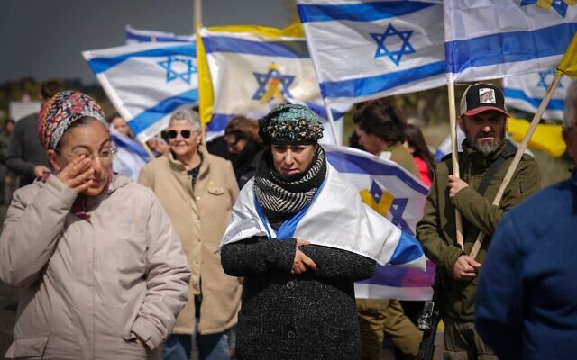إسرائيليون يحملون الأعلام الإسرائيلية وهم يشاهدون موكبا يقل توابيت تحتوي على ما يُعتقد أنها جثامين أربعة رهائن إسرائيليين تم تسليمهم للتو من قبل حركة حماس في غزة بالقرب من كيبوتس رعيم، جنوب إسرائيل، 20 فبراير، 2025. (AP Photo / Ariel Schalit)