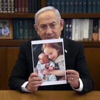 رئيس الوزراء بنيامين نتنياهو يحمل صورة أريئل وكفير بيباس في رسالة فيديو، 21 فبراير، 2025. (Screenshot/GPO)