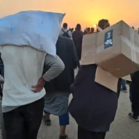 شاب يحمل صندوقا فارغا من مواد الإغاثة من مؤسسة غزة الإنسانية، بينما يسير فلسطينيون نازحون بالقرب من مركز لتوزيع المواد الغذائية في رفح، جنوب قطاع غزة، في 1 يونيو 2025. (AFP)