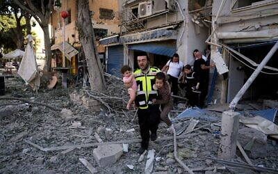 عامل إنقاذ يحمل طفلين أثناء إجلاء السكان من الموقع الذي سقط فيه صاروخ أطلق من إيران على حيفا، 22 يونيو 2025. (AP Photo/Baz Ratner)