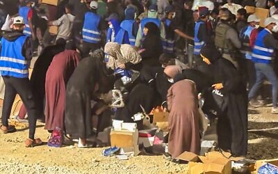 موظفون فلسطينيون محليون تابعون لمؤسسة غزة الإنسانية يرتدون سترات زرقاء يشكلون سلسلة بشرية لحماية النساء المستفيدات من المساعدات في أحد مواقع التوزيع التابعة للمؤسسة في 9 يونيو 2025. (GHF)