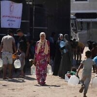 فلسطينيون يحملون حاويات مياه في مخيم للنازحين في دير البلح، قطاع غزة، 7 يوليو/تموز 2025. (صورة أسوشيتد برس/عبد الكريم حنا)