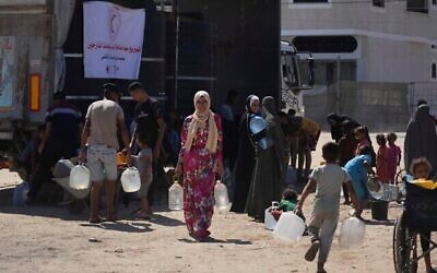 فلسطينيون يحملون حاويات مياه في مخيم للنازحين في دير البلح، قطاع غزة، 7 يوليو/تموز 2025. (صورة أسوشيتد برس/عبد الكريم حنا)