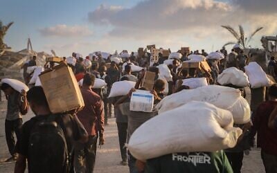 فلسطينيون نازحون يحملون طرودا غذائية وإمدادات من شاحنات مساعدات بالقرب من معبر زيكيم الحدودي بين إسرائيل وبيت لاهيا، في شمال قطاع غزة، 18 أغسطس 2025. (Khalil Kahlout/ Flash90)