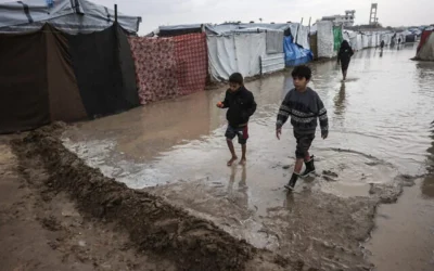 صبيان يسيران عبر زقاق غمرته المياه في مخيم مؤقت يؤوي نازحين فلسطينيين في دير البلح، وسط قطاع غزة، في 11 ديسمبر/كانون الأول 2025. (BASHAR TALEB / AFP)