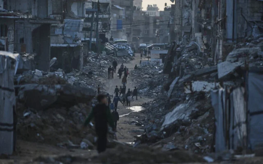 صورة توضيحية: فلسطينيون يسيرون وسط مبانٍ مدمرة في مدينة غزة، شمال قطاع غزة، 15 يناير/كانون الثاني 2026. (AP Photo/Jehad Alshrafi)