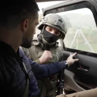 جندي ملثم، تم تحديده باسم مئير، ينظر إلى الكاميرا وهو يفتح باب السيارة التي يجلس فيها مراسل "سي إن إن" جيريمي دايموند، إلى اليسار، محتجزاً في قرية تياسير شمال الضفة الغربية، 26 مارس 2026. (Screen capture: CNN)
