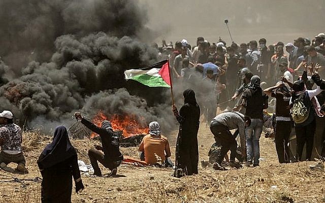 A Palestinian woman holding her national flag looks at clashes with Israeli forces near the border between the Gaza Strip and Israel east of Gaza City on May 14, 2018 (AFP/Mahmud Hams)