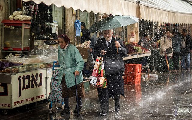 Israelis walking in a downpour rain while shopping at the Mahane Yehuda market in Jerusalem, April 9, 2018. (Liba Farkash/Flash90)