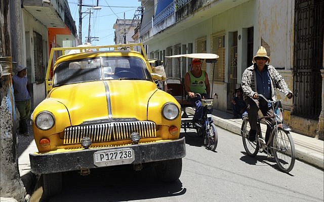 Men riding bicitaxis pass a 1950s auto of unknown origin on a Camagüey side street. (Larry Luxner)