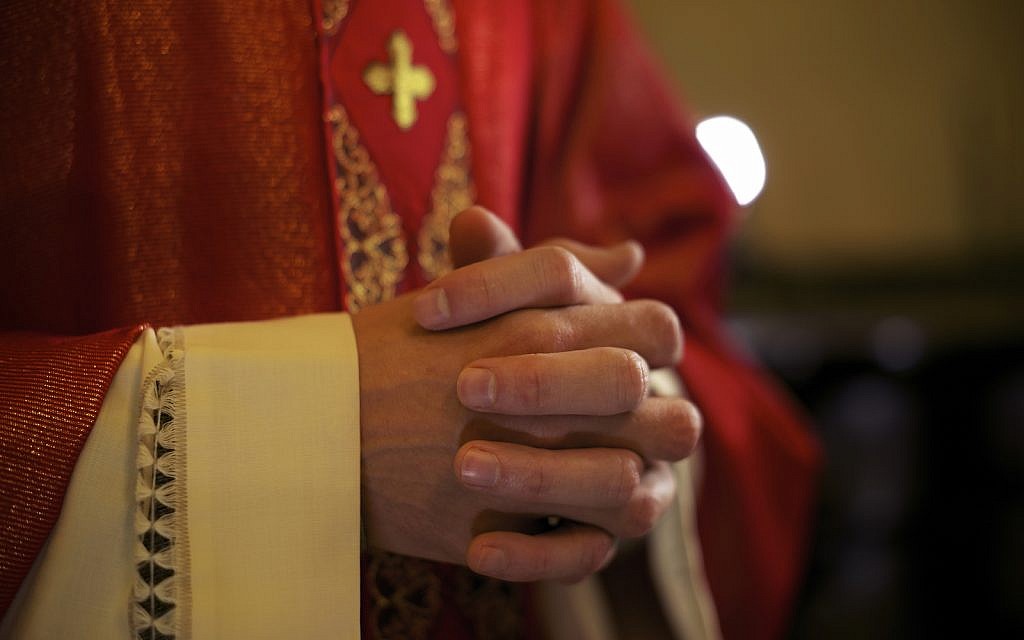 Catholic priest on altar praying with hands joined during mass service in church (iStock)