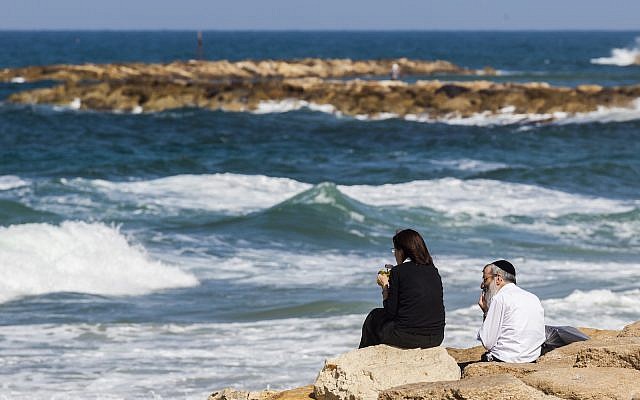 Illustrative: Couple sits on rocks by the sea in Tel Aviv (iStock) Illustrative: Couple sits on rocks by the sea in Tel Aviv (iStock)