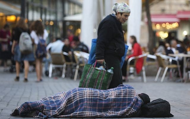 Illustrative. People walk by a homeless man sleeping on the street, near cafes in the center of Jerusalem. November 10, 2013. (Nati Shohat/ FLASH90)
