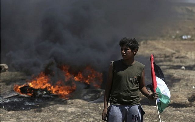 A boy holds a Palestinian flag in front of burning tires during a protest at the Gaza Strip's border with Israel, Monday, May 14, 2018.  (AP Photo/Khalil Hamra via Jewish News)