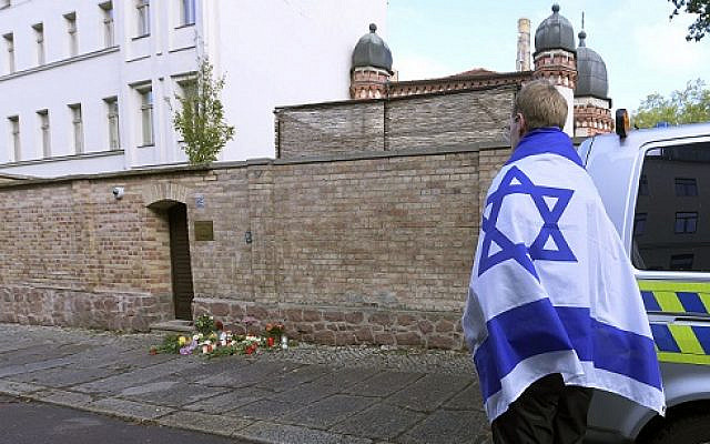 A person with a flag of Israel stands next to flowers and candles in front of a synagogue in Halle, Germany, following a terror shooting on Yom Kippur (AP Photo/Jens Meyer via Jewish News) A person with a flag of Israel stands next to flowers and candles in front of a synagogue in Halle, Germany, following a terror shooting on Yom Kippur (AP Photo/Jens Meyer via Jewish News)