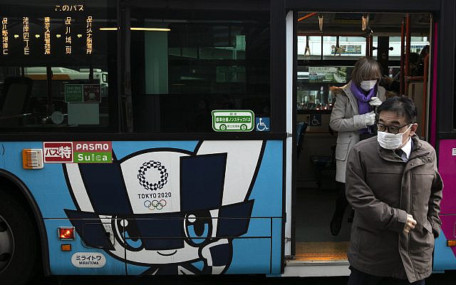 Passengers wearing masks get off a bus with the livery of Miraitowa, the official mascot of the Tokyo 2020 Olympics, in Tokyo, Thursday, March 5, 2020. (AP Photo/Jae C. Hong)