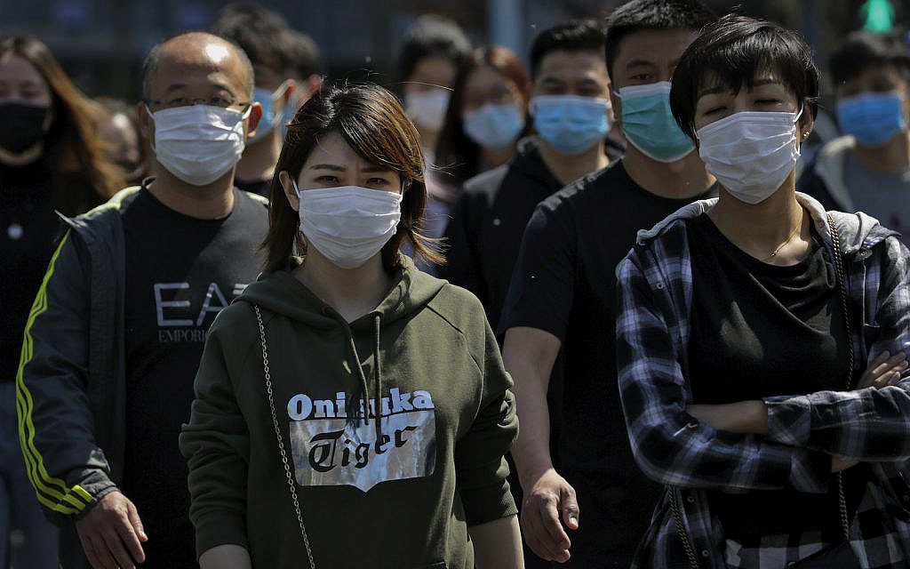 People wearing protective face masks to prevent the spread of the new coronavirus walk across a street in Beijing, Sunday, April 12, 2020. (AP Photo/Andy Wong)