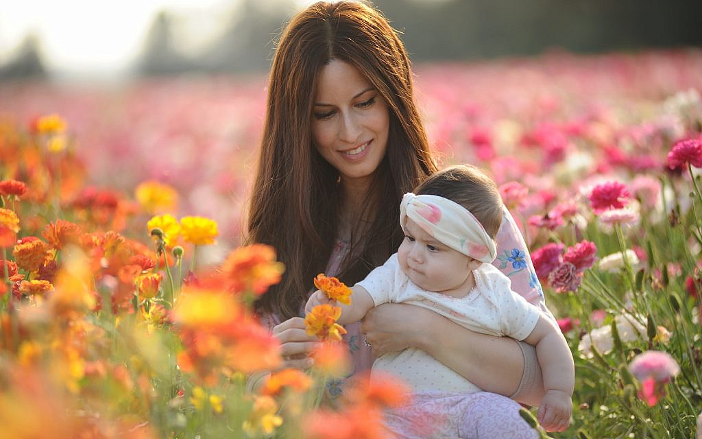 A mother holds her baby at a field of buttercup flowers near Kibbutz Nir Itzhak in southern Israel, on April 26, 2020.(Mendy Hechtman/Flash90)