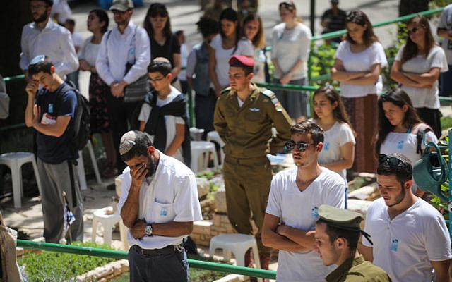 In a different year, when social distancing was not yet relevant: people stand in silence next to graves of Israeli soldiers at the Mt. Herzl military cemetery in Jerusalem, as a two-minute siren sounded across Israel, marking Memorial Day which commemorates Israel's fallen soldiers and victims of terror. April 18, 2018. (Miriam Alster/ Flash90) In a different year, when social distancing was not yet relevant: people stand in silence next to graves of Israeli soldiers at the Mt. Herzl military cemetery in Jerusalem, as a two-minute siren sounded across Israel, marking Memorial Day which commemorates Israel's fallen soldiers and victims of terror. April 18, 2018. (Miriam Alster/ Flash90)