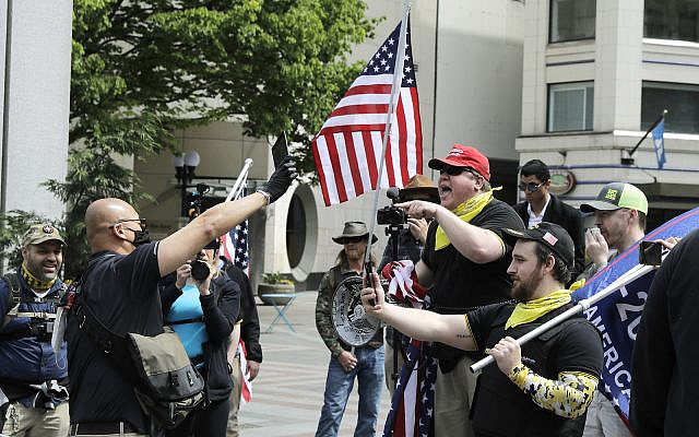 Members of a group wearing shirts with the logo of the far-right Proud Boys group at right, argue with a counter protester during a small protest against Washington state's stay-at-home orders, Friday, May 1, 2020, in downtown Seattle. (AP Photo/Ted S. Warren)