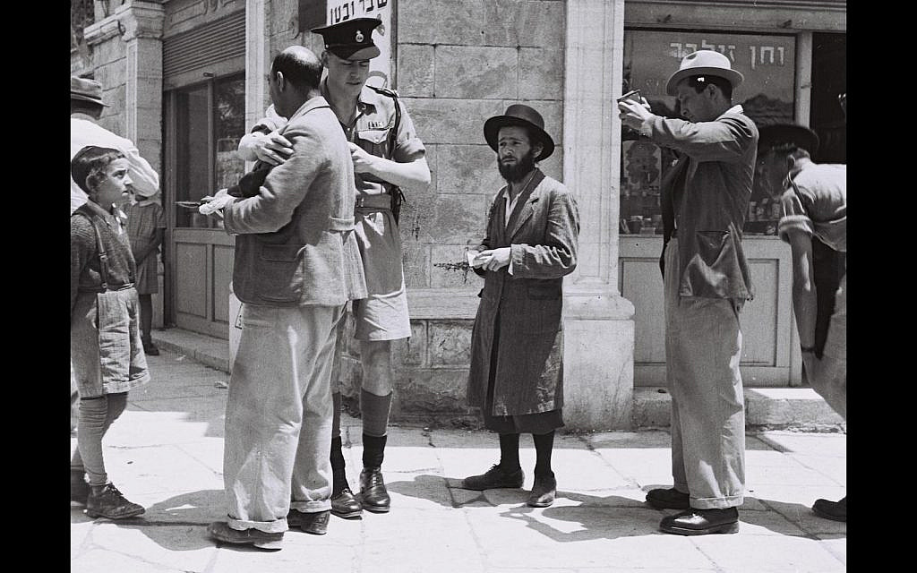 A British policeman checking papers of passers by on a street in Jerusalem, during the British Mandate, 1947 (Wiki Cc)