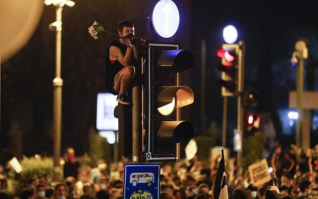 A protester holds flowers and sits on a traffic signal during a demonstration against the Prime Minister Benjamin Netanyahu, in Jerusalem, on July 23, 2020. (MENAHEM KAHANA / AFP) A protester holds flowers and sits on a traffic signal during a demonstration against the Prime Minister Benjamin Netanyahu, in Jerusalem, on July 23, 2020. (MENAHEM KAHANA / AFP)